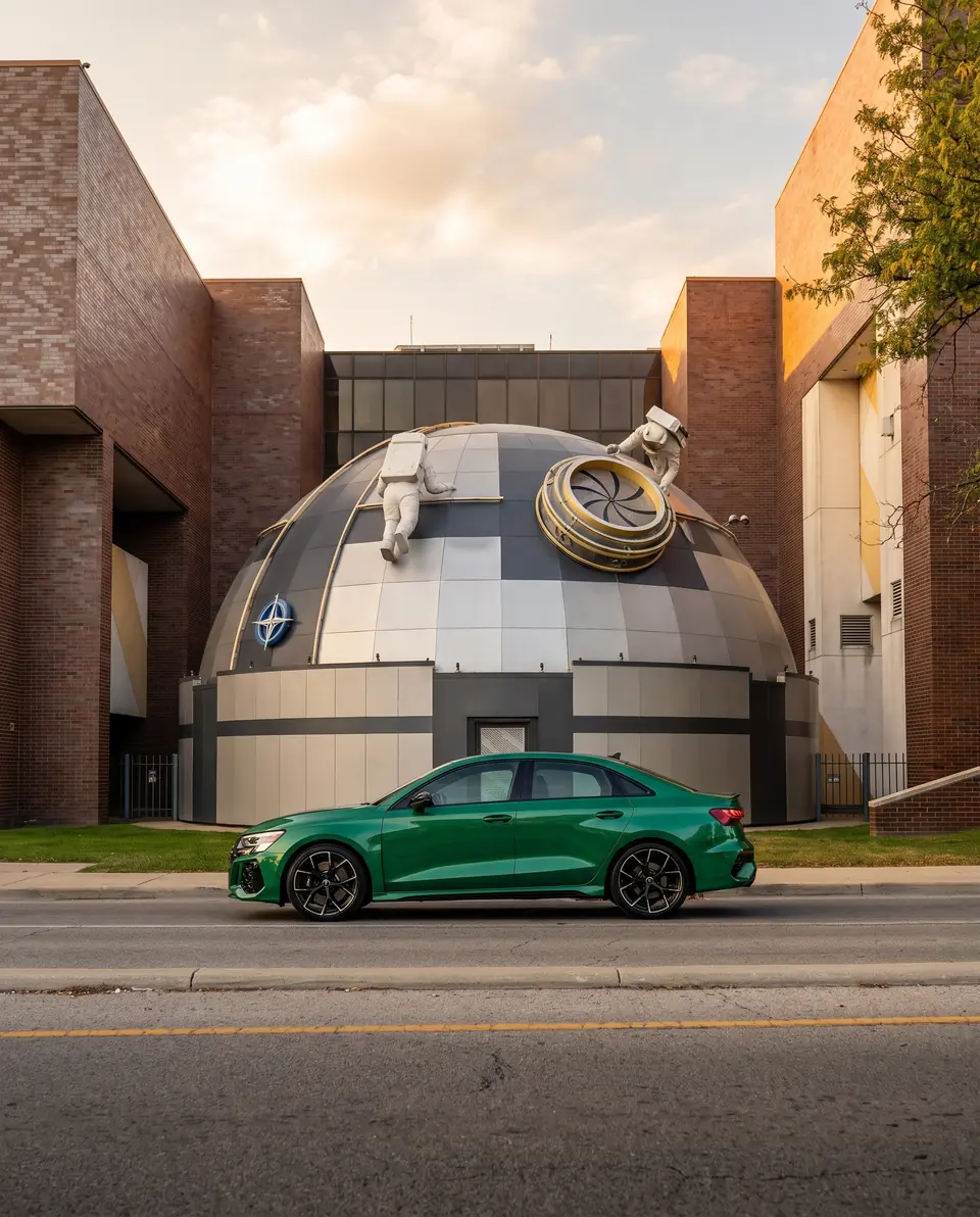 A green sports saloon in front of a domed building with astronaut sculptures on the roof