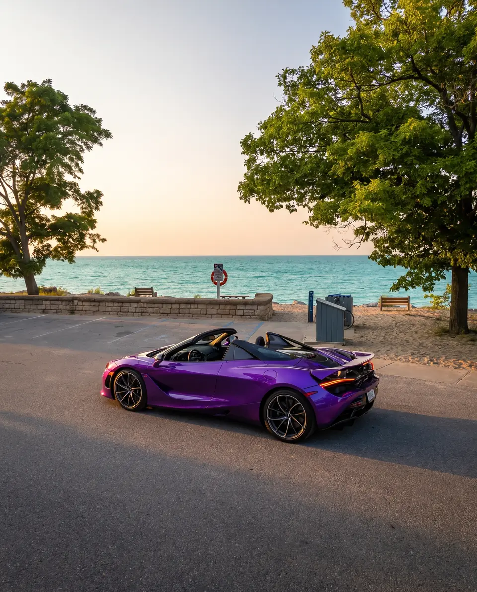 A purple convertible supercar parked by a beach with turquoise water at golden hour