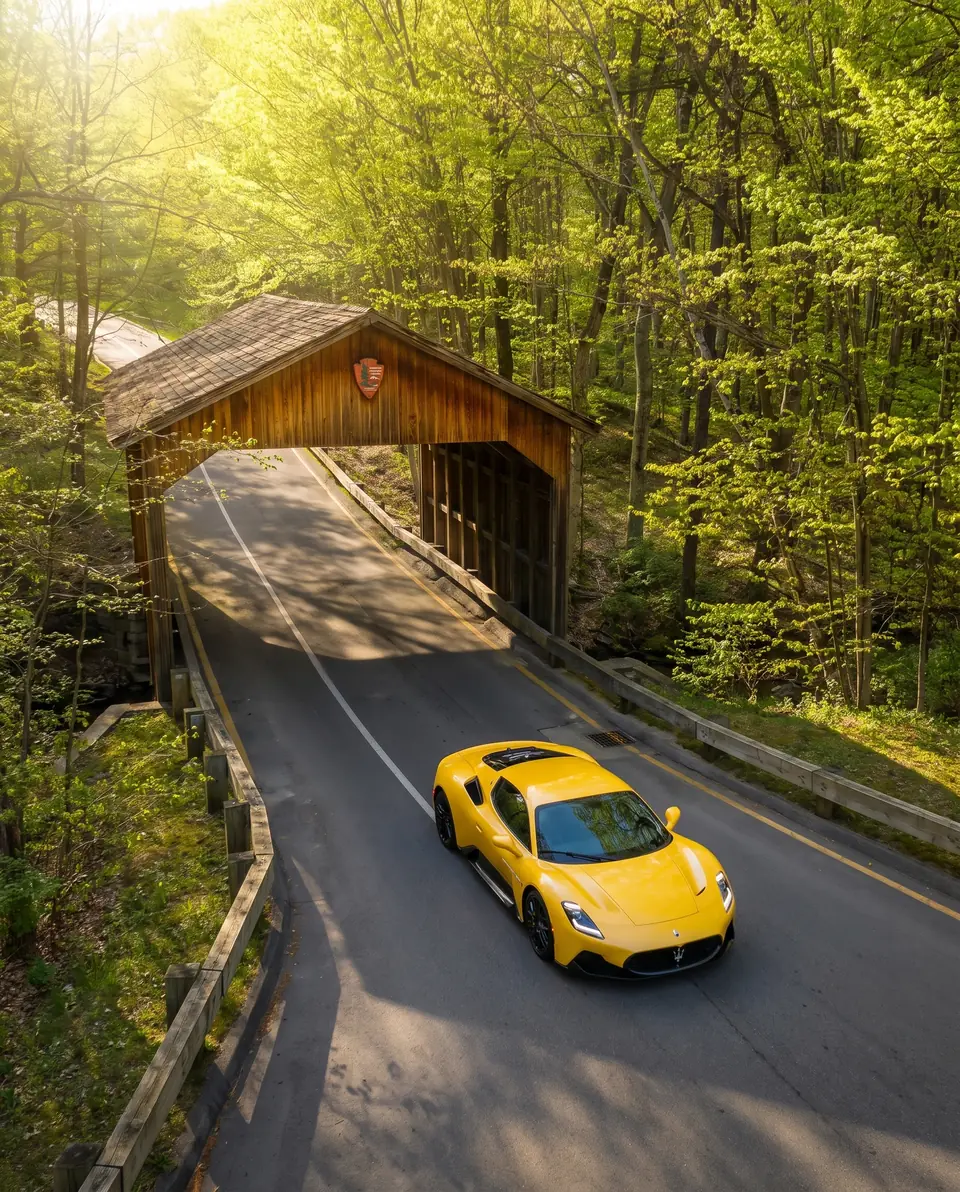A yellow sports car on a forest road coming out of a wooden covered bridge
