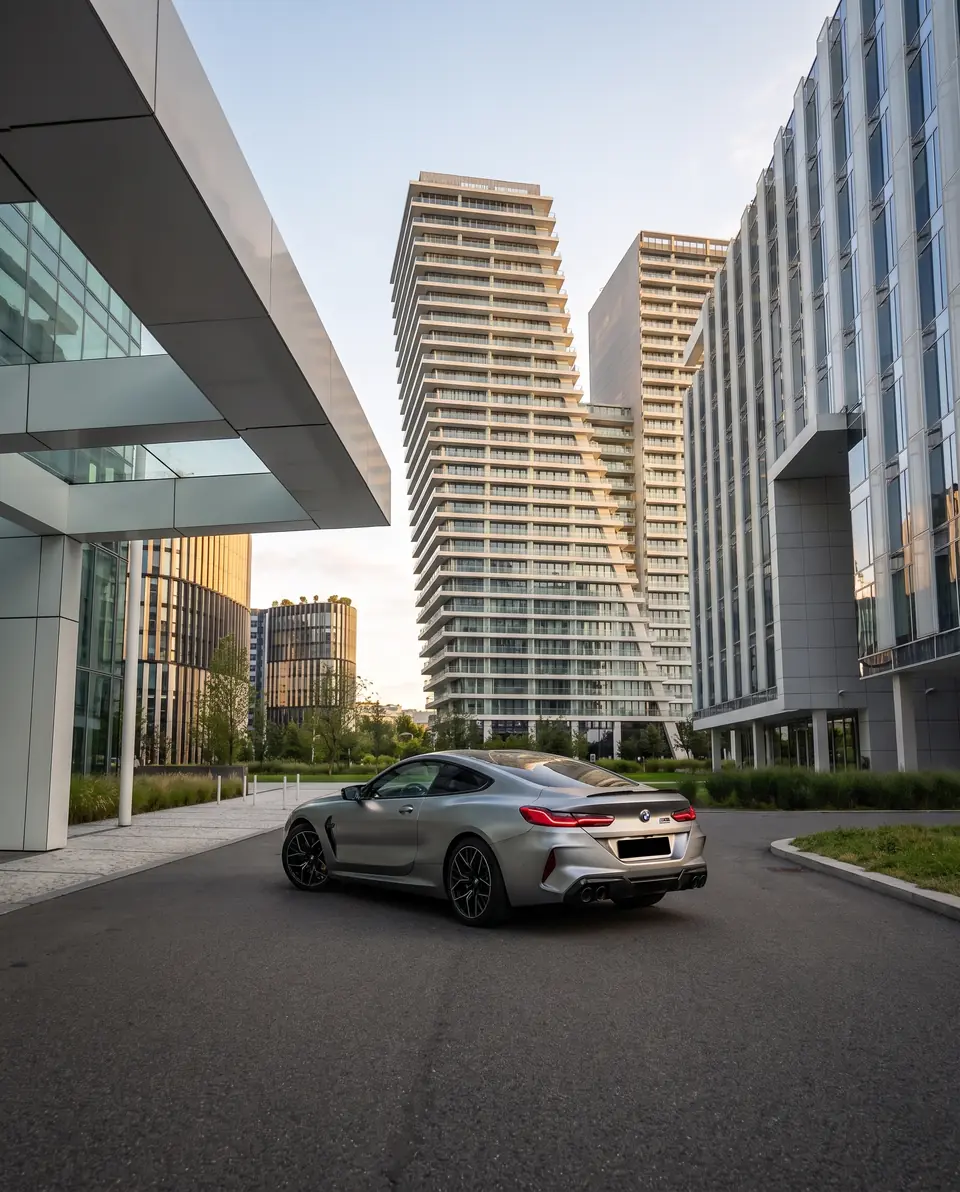 A grey sports coupe in a plaza between modern glass office and apartment towers