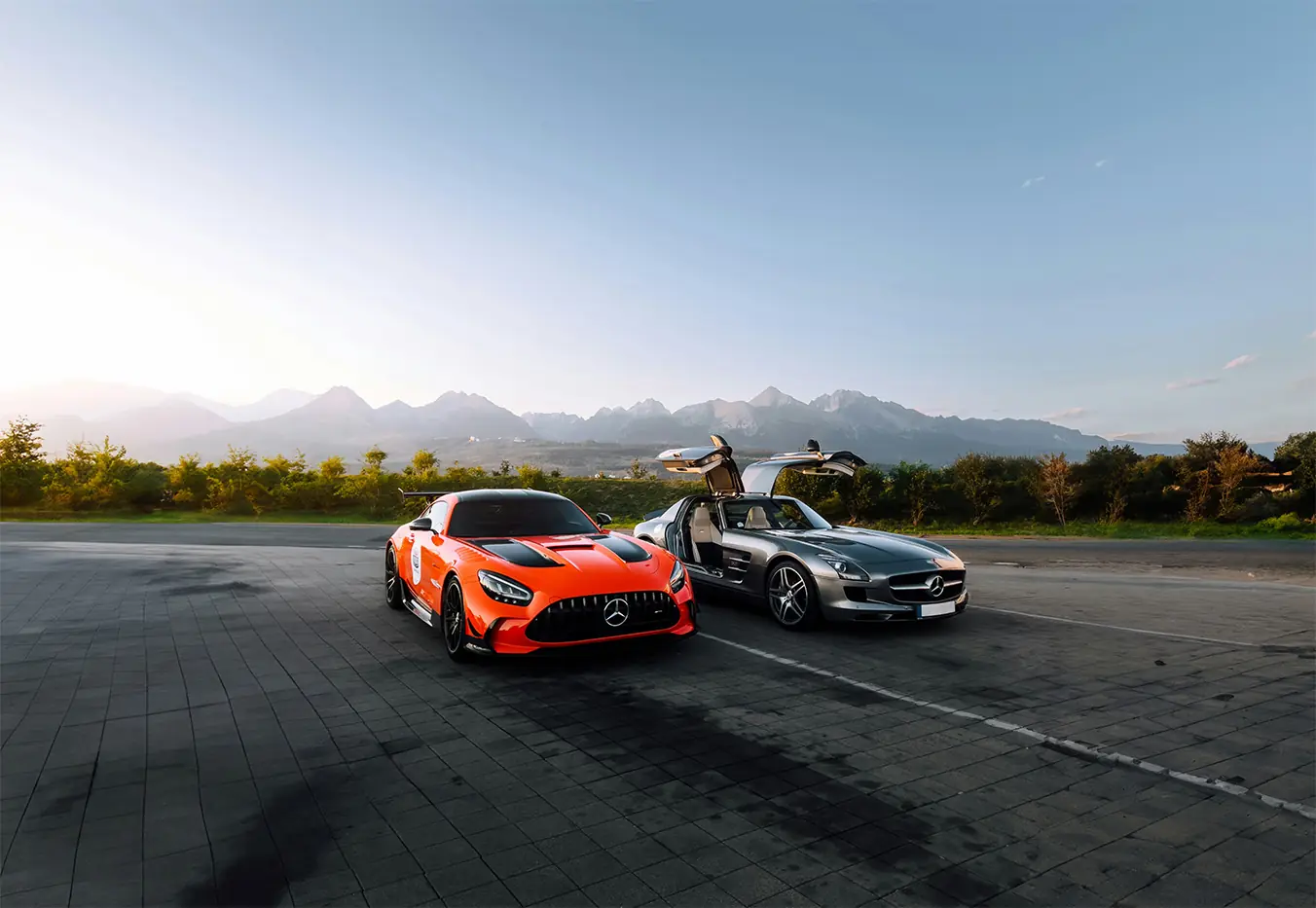 Two sports cars parked below a mountain range as the sun goes down